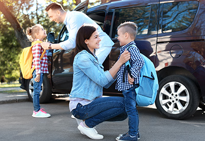 Family preparing for a school drop off with two children smiling by a parked car showcasing backpacks and school spirit for grade 9