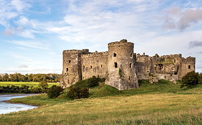 scenic view of an old stone castle surrounded by lush green grass and a river under a blue sky with clouds highlighting historic architecture and the number 9 in its unique features