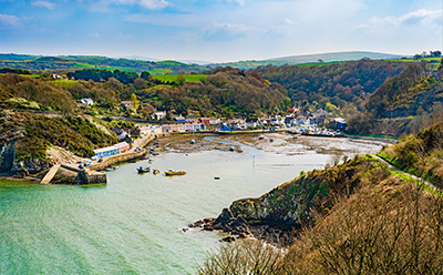 scenic coastal view of a small harbor surrounded by hills and greenery with boats in the water and colorful buildings along the shore showcasing natural beauty and four seasons